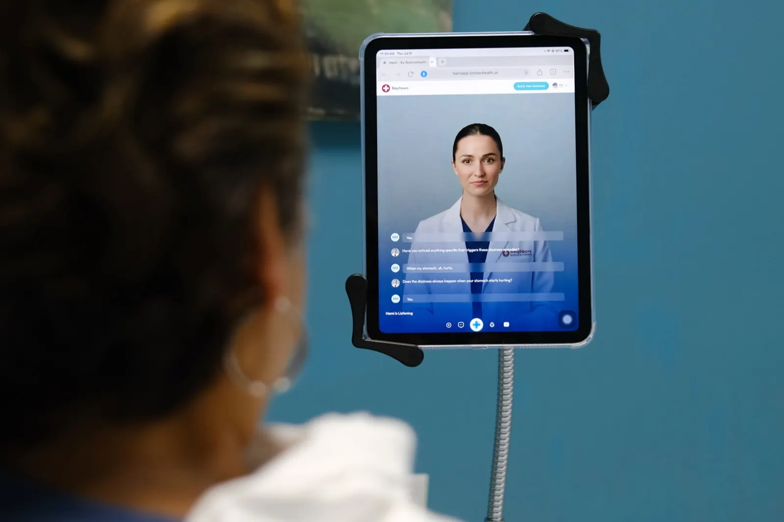 A patient in an exam room talking with an AI patient-history assistant on a tablet